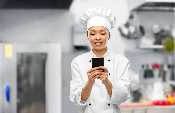 Chef mujer sonriente con teléfono inteligente en la cocina —  Fotos de Stock