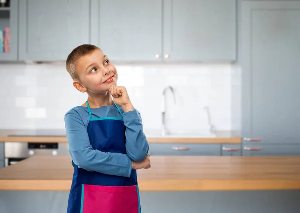 Lächelnder kleiner Junge in Schürze denkt in Küche — Stockfoto