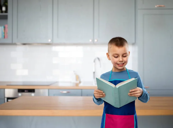 Sorrindo menino no avental leitura livro cozinheiro — Fotografia de Stock