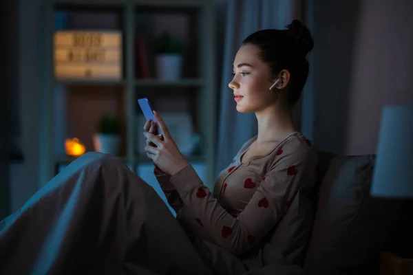 Gadis remaja dengan telepon dan earphone di tempat tidur — Stok Foto
