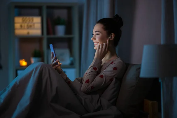 Adolescente con teléfono y auriculares en la cama por la noche — Foto de Stock