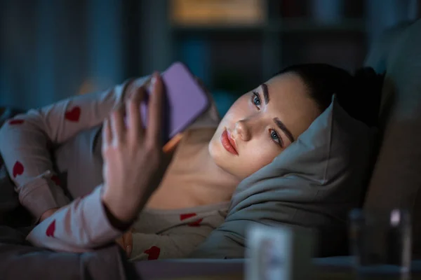 Dospívající dívka s smartphone ležící v posteli v noci — Stock fotografie