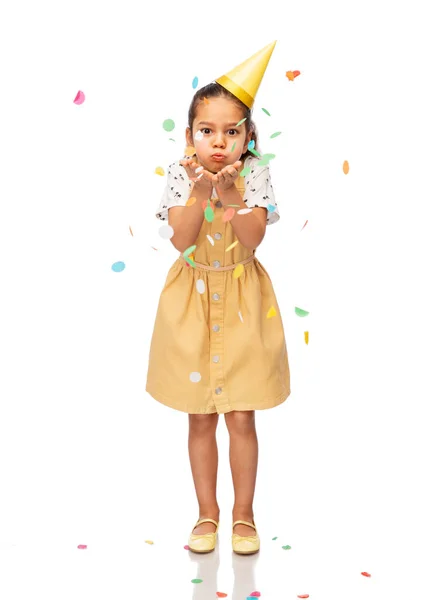 Flicka i födelsedagskalas hatt blåser till konfetti — Stockfoto