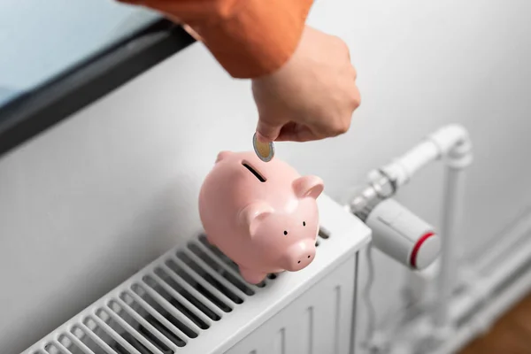 Mão colocando moeda no banco porquinho no radiador — Fotografia de Stock