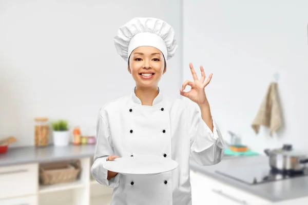 Женщина шеф-повар держит пустую тарелку и показывает хорошо — стоковое фото
