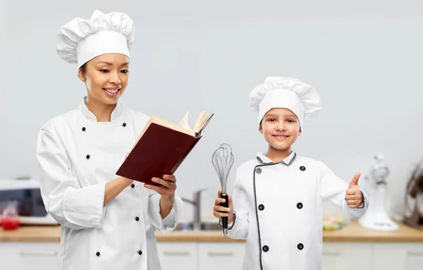 Chef feminino com livro de cozinha e menina na cozinha — Fotografia de Stock