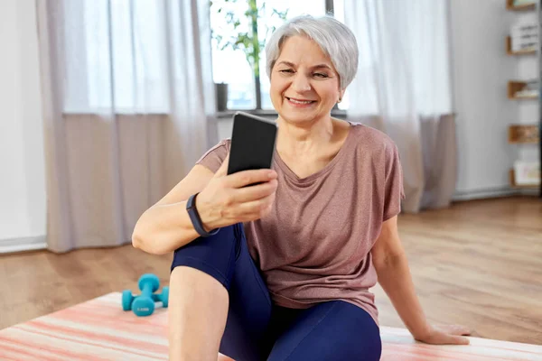 Ηλικιωμένη γυναίκα με άσκηση smartphone στο σπίτι — Φωτογραφία Αρχείου