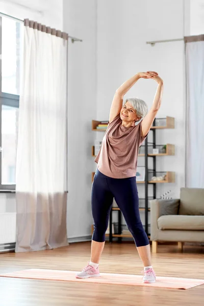 Usmívající se starší žena cvičení na podložce doma — Stock fotografie