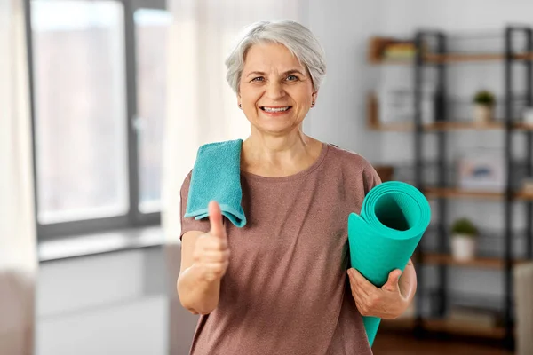 Gammal kvinna med yogamatta och handduk visar tummen upp Stockbild