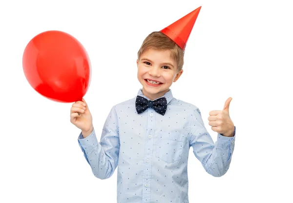 Menino em boné de aniversário com balão mostrando polegares para cima — Fotografia de Stock