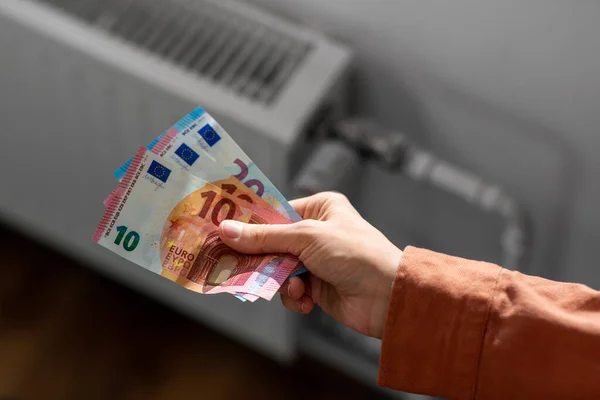 Close up de mão com dinheiro no radiador em casa — Fotografia de Stock