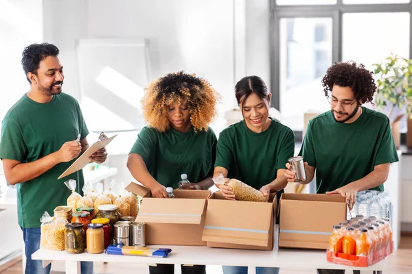 Gelukkige vrijwilligers die voedsel in donatiedozen verpakken Stockfoto