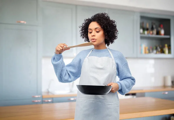 Mulher com frigideira degustação de alimentos na cozinha Fotografias De Stock Royalty-Free