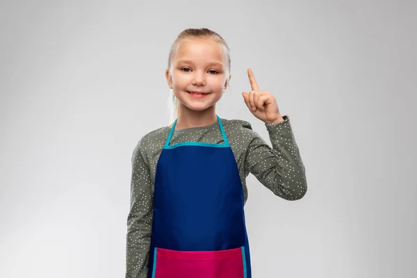 Sorrindo menina no avental apontando dedo para cima — Fotografia de Stock