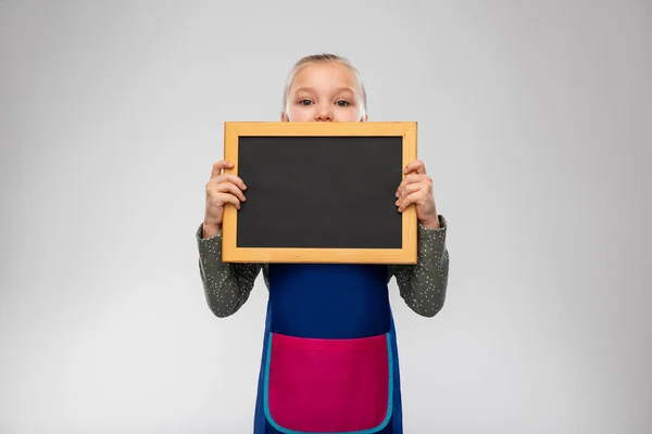 Niña sonriente en delantal sosteniendo pizarra —  Fotos de Stock