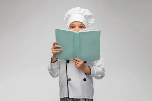 Little girl in chefs toque reading cook book — Stock Photo, Image