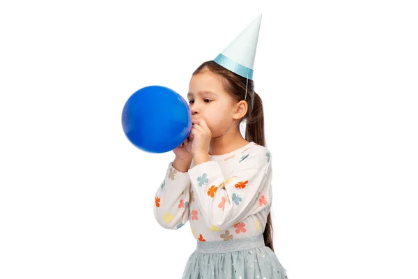 Holčička v narozeninové párty klobouk foukání balón — Stock fotografie