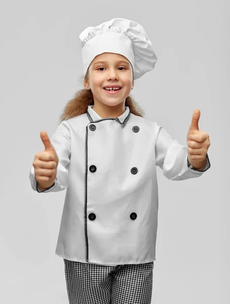Маленькая девочка в токе шеф-повара показывает большие пальцы вверх — стоковое фото