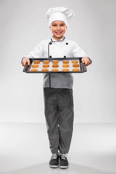 Menino em chefs toque com biscoitos na bandeja do forno — Fotografia de Stock