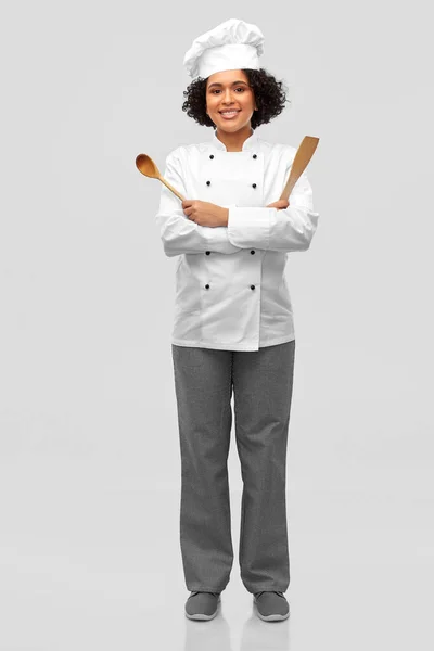 Улыбающаяся женщина-шеф-повар с деревянной ложкой и лопаткой — стоковое фото