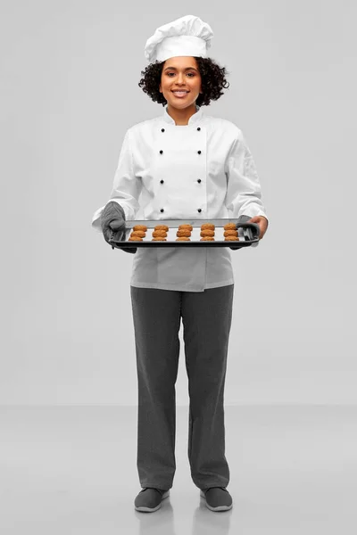 Happy female chef with cookies on oven tray — Stock Photo, Image