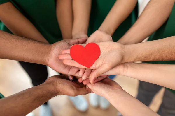 Close up of volunteerss hands holding red heart — Stock Photo, Image