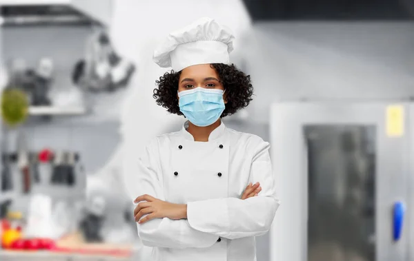 Female chef in medical mask and toque in kitchen — Stockfoto