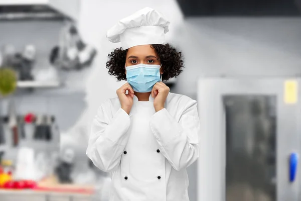 Female chef in medical mask and toque in kitchen — Stockfoto