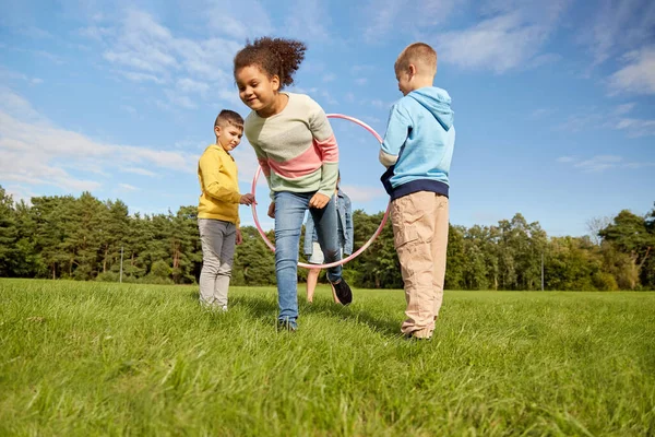 Crianças felizes jogando jogo com hula hoop no parque — Fotografia de Stock