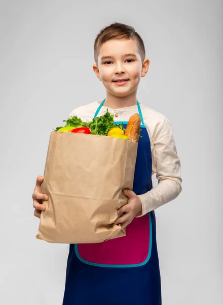 Smiling little boy in apron with food in paper bag — Foto Stock
