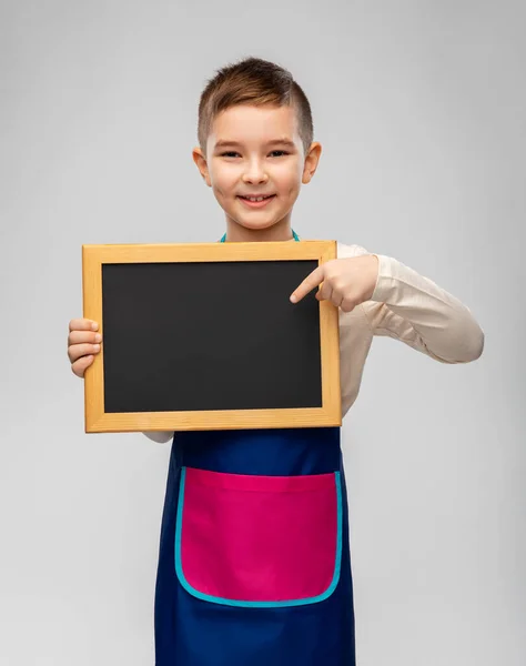 Smiling little boy in apron holding chalkboard — Stock Photo, Image