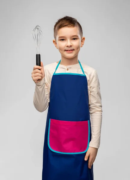 Smiling little boy in apron holding whisk — Stock Photo, Image