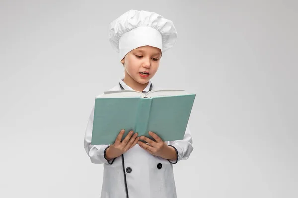 Menina em chefs toque leitura livro cozinheiro — Fotografia de Stock