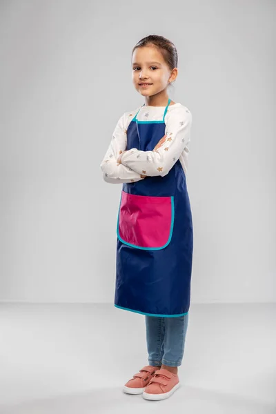 Sorridente bambina in grembiule con le braccia incrociate — Foto Stock