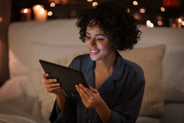 Lycklig kvinna med tablett dator sittande i sängen på natten — Stockfoto