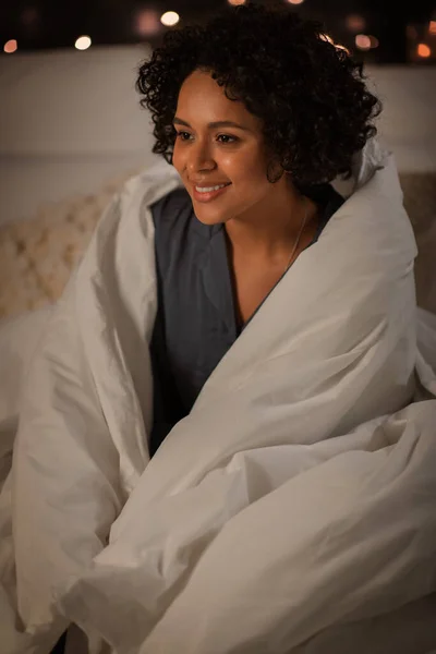 Женщина, завернутая в одеяло, сидит ночью в постели — стоковое фото