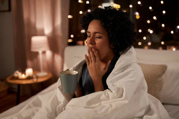 Mujer cansada con café bostezando en la cama por la noche —  Fotos de Stock