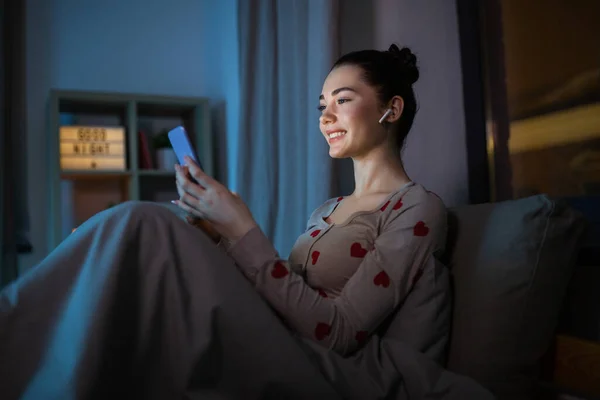 Tinédzser lány telefonnal és fülhallgatóval az ágyban éjszaka — Stock Fotó