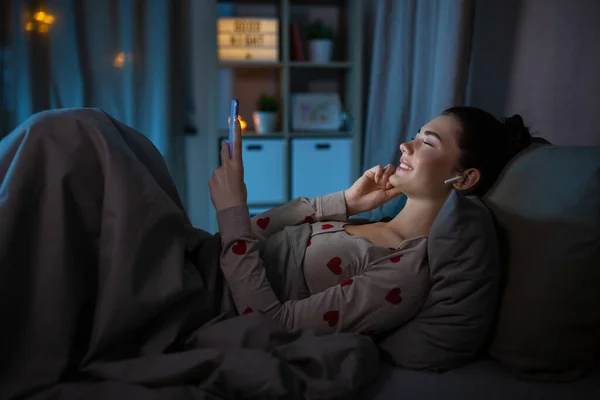 Gadis muda yang bahagia dengan telepon dan earphone di tempat tidur — Stok Foto