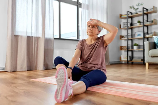 Mujer mayor cansada haciendo ejercicio en la alfombra en casa — Foto de Stock