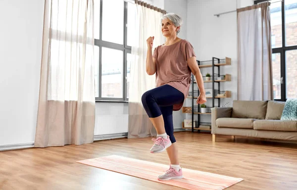 Mujer mayor sonriente haciendo ejercicio en la alfombra en casa — Foto de Stock