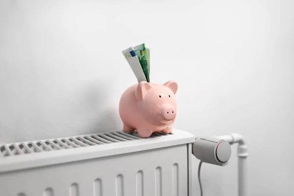 Spaarvarken bank met geld op radiator thuis — Stockfoto