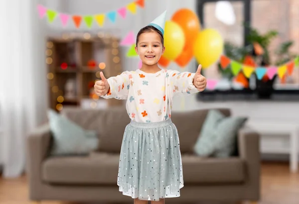 Menina feliz em chapéu de festa de aniversário mostrando polegares para cima — Fotografia de Stock