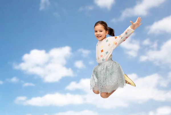 Glad liten flicka hoppar över blå himmel och moln — Stockfoto