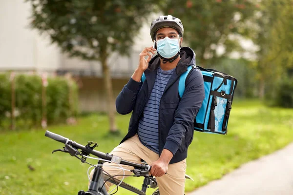 Entrega homem em máscara com smatphone andar de bicicleta Imagem De Stock