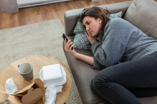 Stressed woman with smartphone on sofa at home — Stock fotografie
