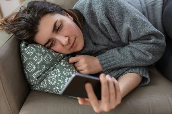 Stressed woman with smartphone on sofa at home — Stock fotografie