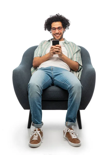 스마트폰을 들고 의자에 앉아 미소짓는 젊은 남자 — 스톡 사진