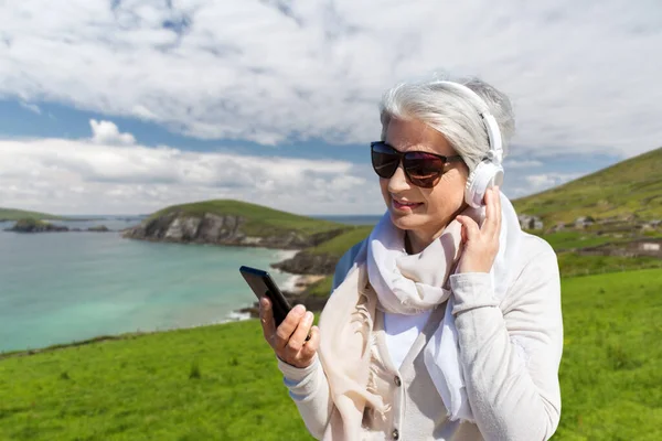 Alte Frau mit Kopfhörer und Smartphone am Strand — Stockfoto