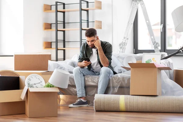 Hombre triste con teléfono inteligente y cajas de mudanza a casa —  Fotos de Stock
